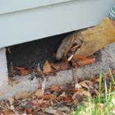 An Xtreme Home Improvement employee performing spring outdoor home maintenance by clearing foundation vents
