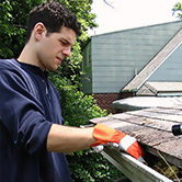 An Xtreme Home Improvement employee performs spring outdoor home maintenance by cleaning roof rain gutters